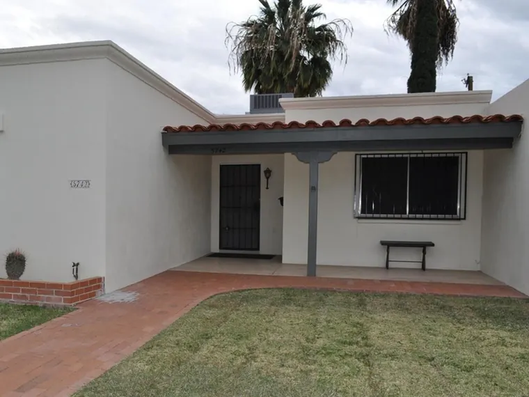 Single story white stucco townhome with a red tile porch roof, a brick walk and tall palms at 5742 E Grant Rd, Tucson, Arizona