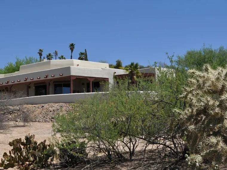 Pueblo style stucco home with a long covered patio on a Sonoran Desert hillside with cholla and mesquite at 7937 N Porto Fino Cir, Tucson, Arizona